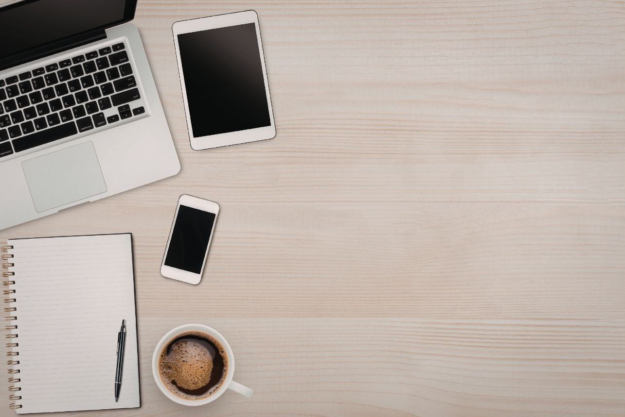 Schreibtisch mit Handy, Tablet, Laptop, Kaffeetasse und Notizblock.